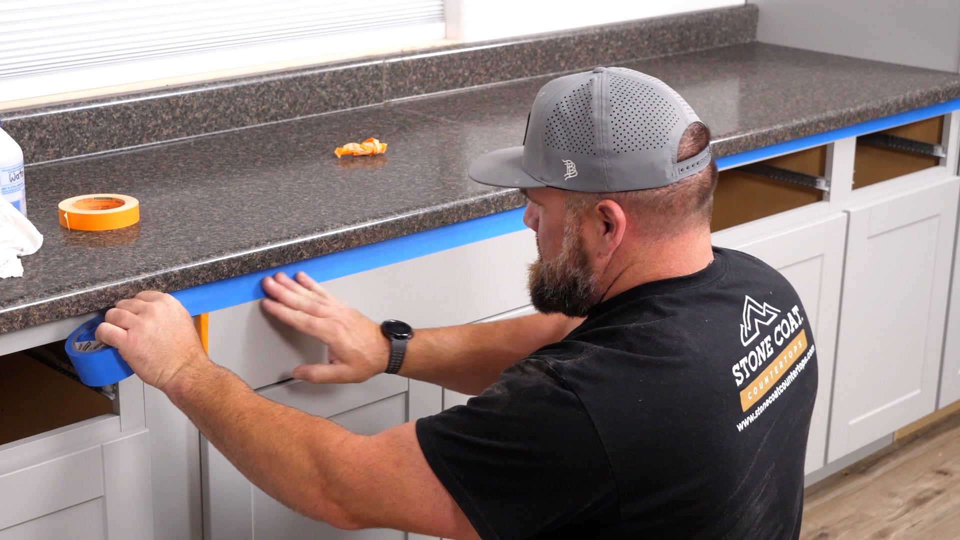 Man aligning blue masking tape below a countertop