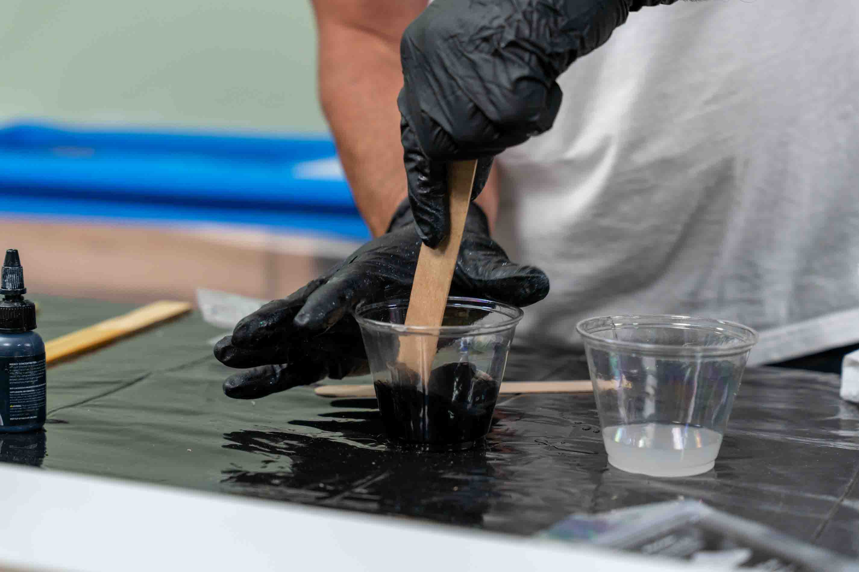 Stirring black tinted apex polyaspartic in a small clear plastic cup.