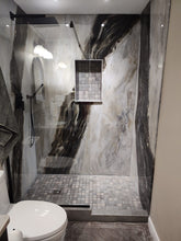 Black, white, and grey marbled shower with glass slider door and grey tiled insert shelf