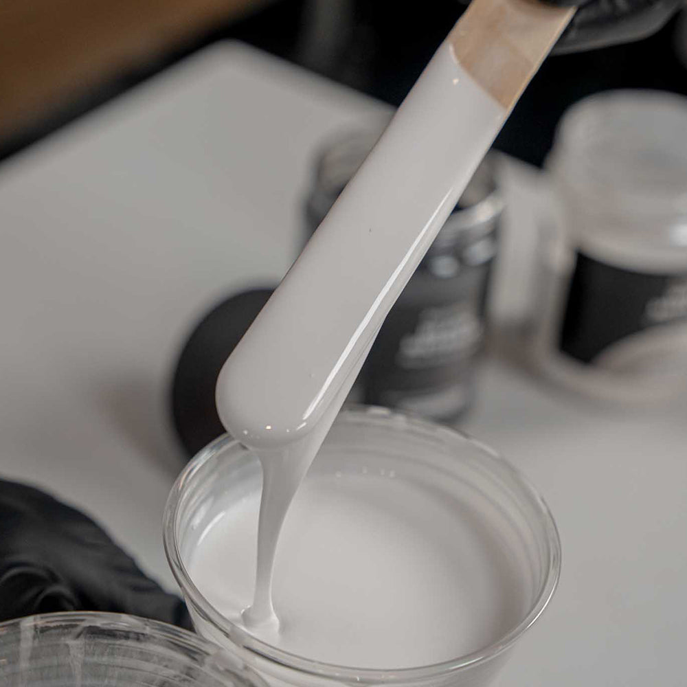 White tinted apex stone coat polyaspartic being stirred with a wooden-handled brush in a clear container.