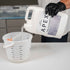 Person pouring Apex Polyaspartic coating into a measuring container.