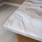 A close-up of a polished stone countertop with a white and beige marbled pattern, installed on a wooden table in a modern room with light gray flooring.