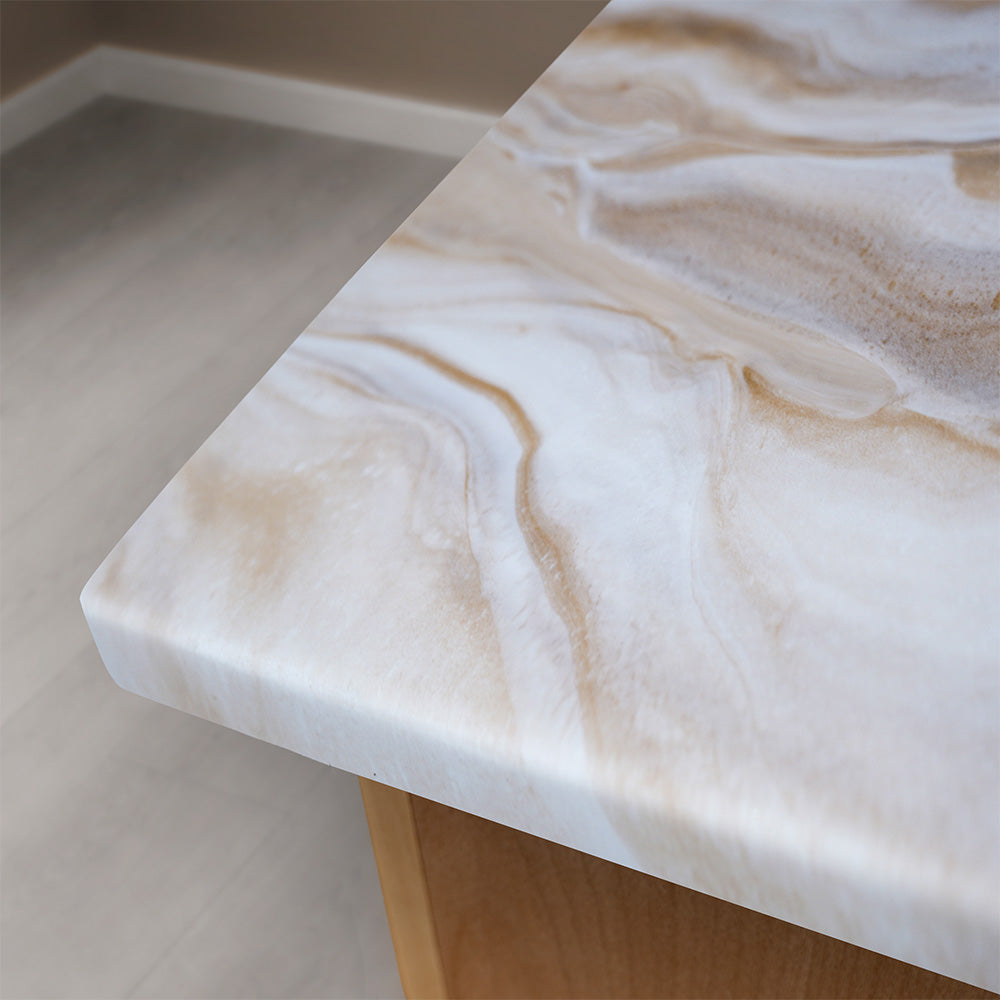 A close-up of a polished stone countertop with a white and beige marbled pattern, installed on a wooden table in a modern room with light gray flooring.
