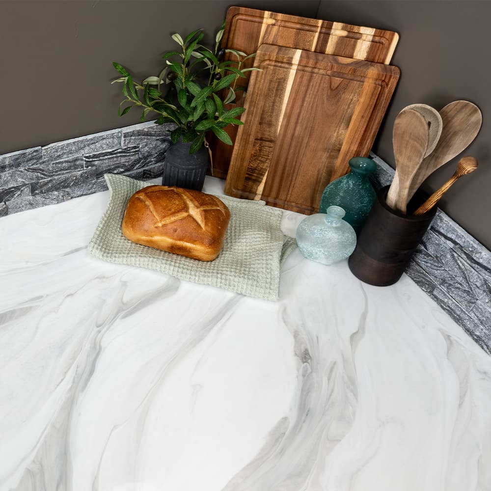Wooden cutting boards, loaf of bread, and kitchen utensils on a marble surface.