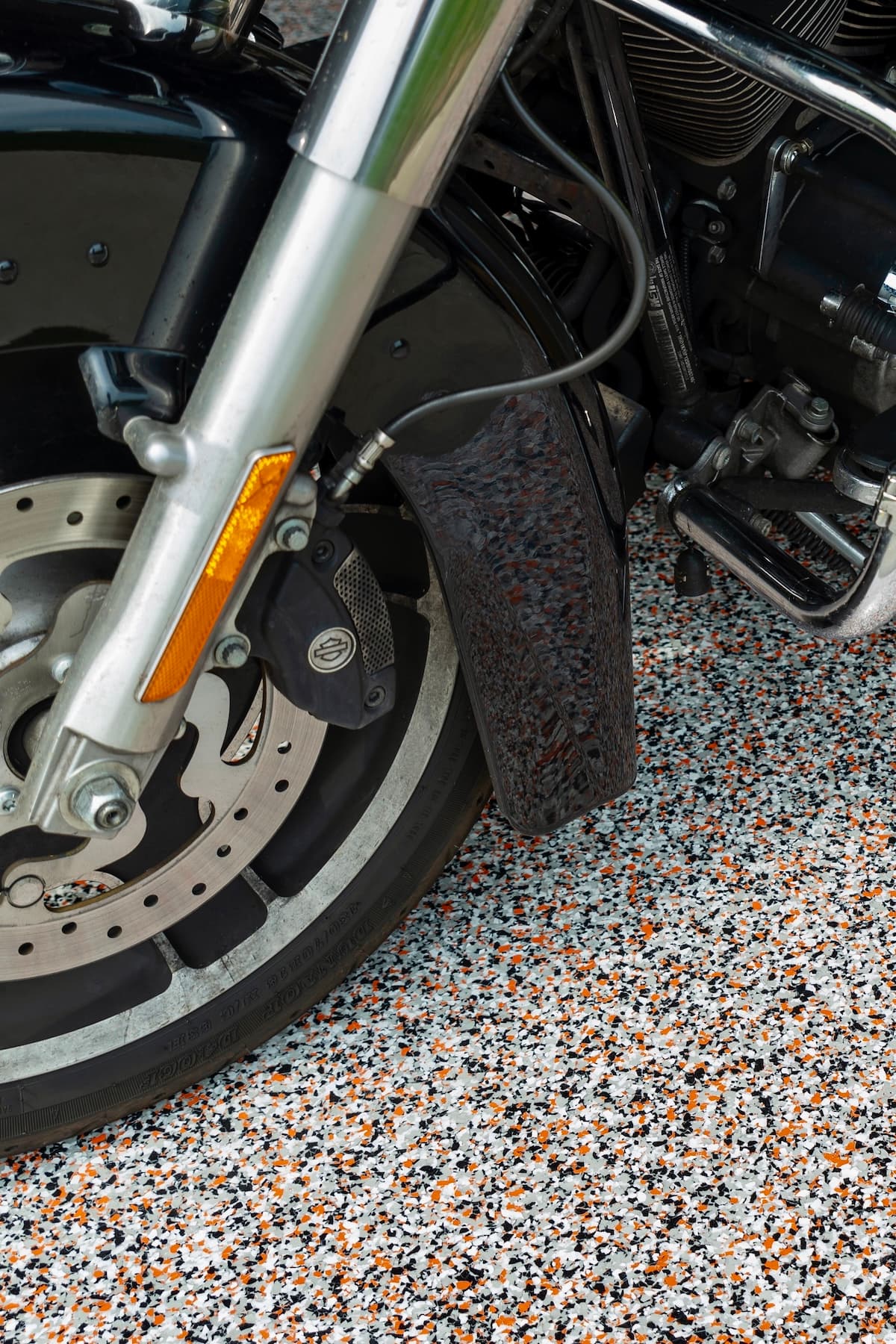 Close-up of a motorcycle's front wheel and suspension on a speckled flake garage floor.