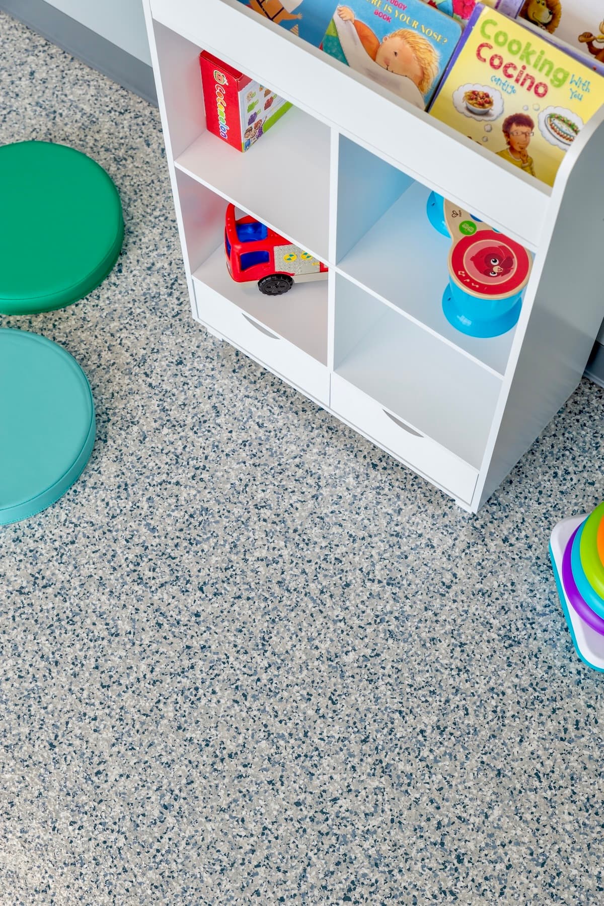 White children's bookshelf with toys on a speckled gray flake floor.