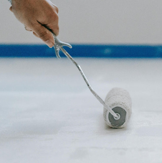 A hand using a roller to paint on primer